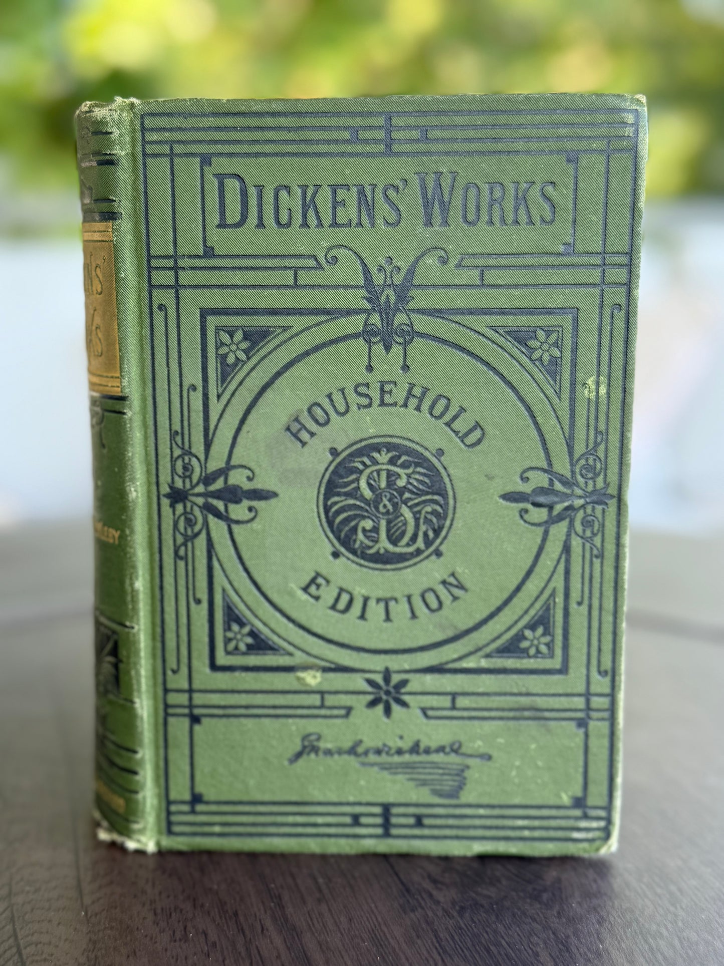 Vintage book titled 'Dickens' Works Household Edition' with decorative cover on a wooden surface.