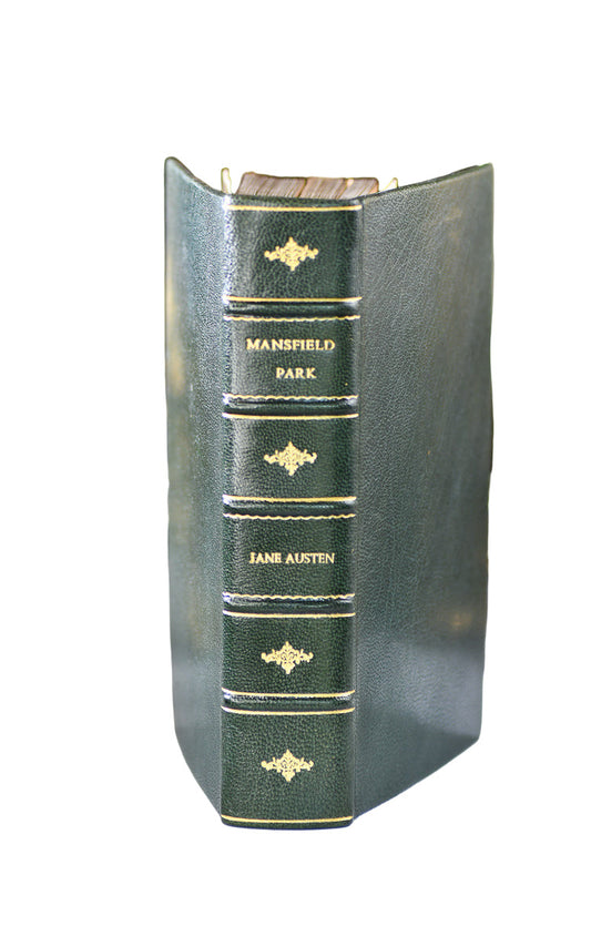 Green book titled 'Mansfield Park' by Jane Austen with gold embossed text, placed on a reflective surface with decorative background.