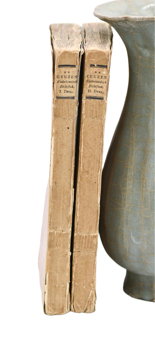 Two old books with hard covers, slightly damaged, one standing next to a ceramic vase.