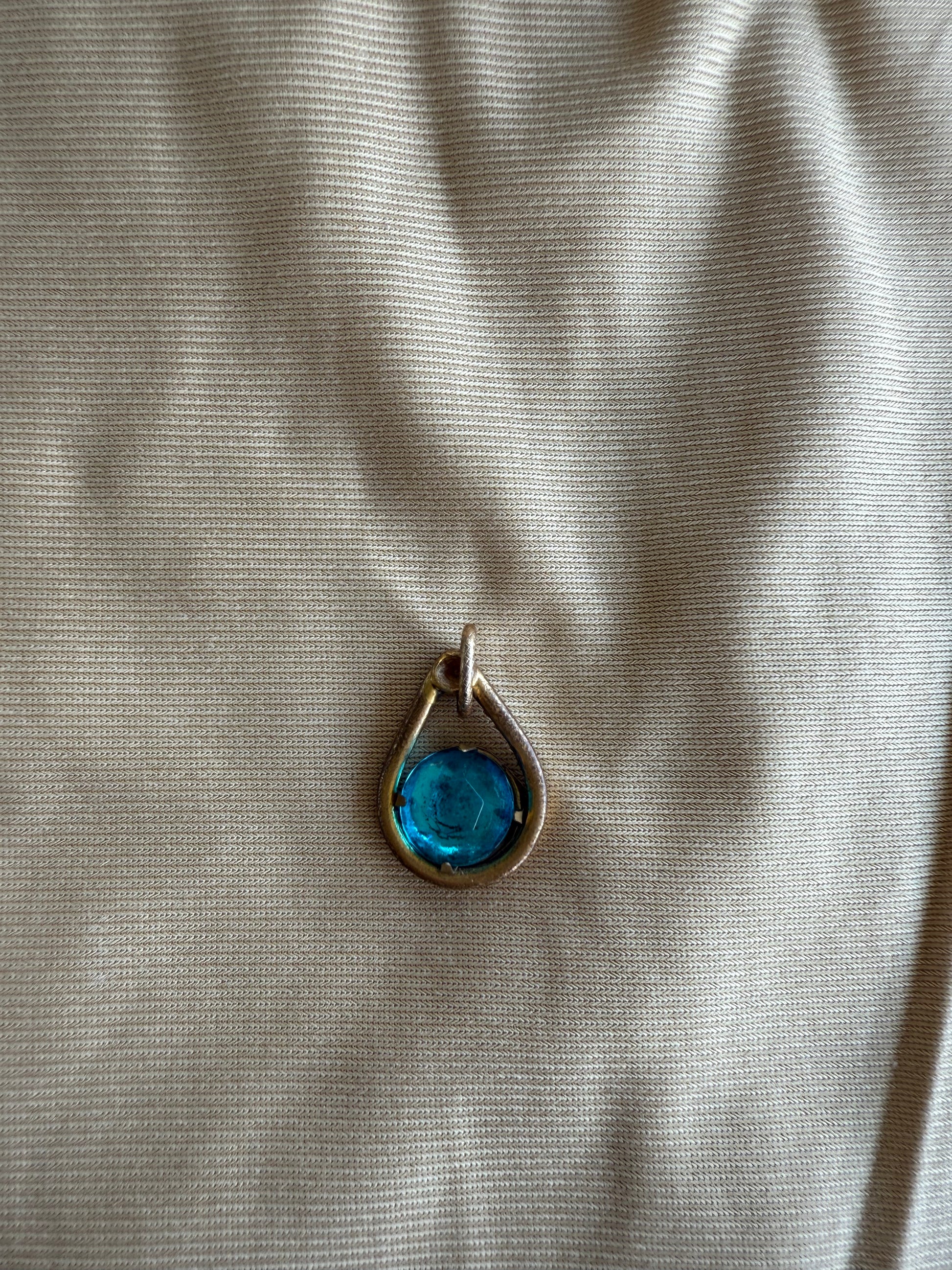 Teardrop-shaped pendant with a green stone on a beige fabric background