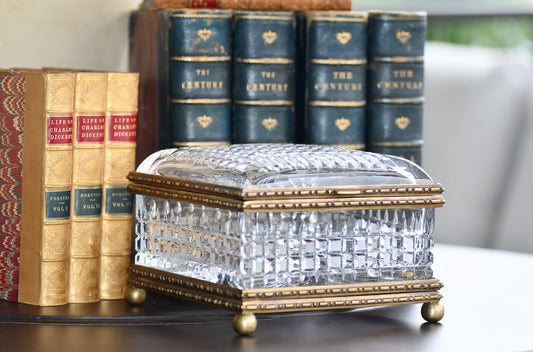 Decorative crystal box with gold accents on a surface with books in the background