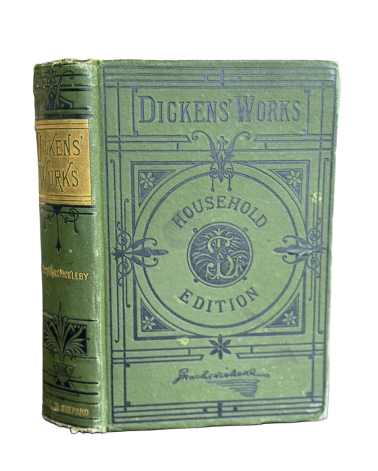 Vintage green book titled 'Dickens' Works' with decorative cover on a wooden surface.