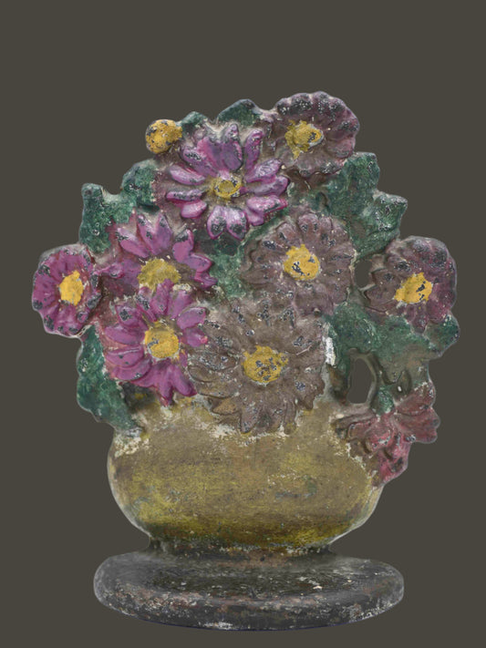 A vintage floral doorstop featuring pink and brown daisies in a gold vase with a white area in the center of the largest brown flower. The base is brown with light chipping, and the back is gold.