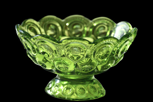 A vintage green glass bowl with a pattern of moons and stars, displayed in sunlight which highlights its bright color and reflective surface.