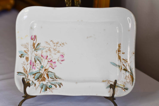 A vintage white ceramic rectangular serving plate with floral patterns on the side, displaying light scratches and spots indicative of its age.
