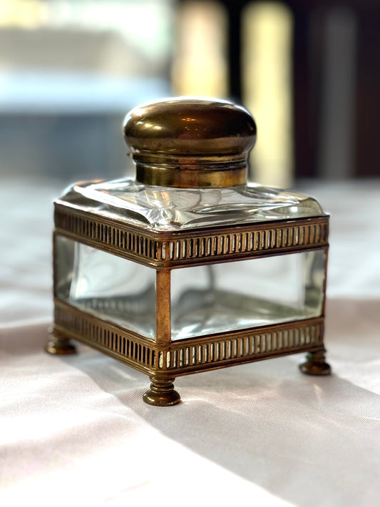 Clear glass inkwell with brass lid on a white surface